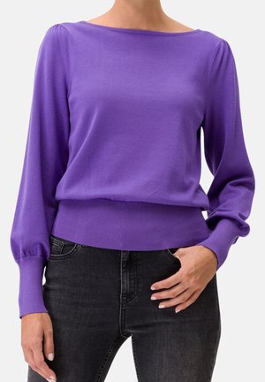 Pull en tricot violet avec un col bateau, de longues manches bouffantes et un ourlet côtelé. Associé à un jean noir, mettant en valeur son design décontracté.