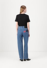 Svart kortermet skjorte med blå vide denimjeans som har røde og svarte trykte mønstre på baklommen. Elegant, avslappet utseende.
