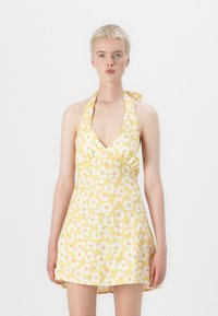 Geel bloemen halterjurk met een diepe V-hals, witte bloemen met oranje accenten en een licht uitlopende rok. Zachte textuurstof.