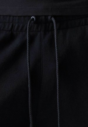 Pantalones o pantalones cortos de tela negra con cintura elástica y cordones negros atados a través de ojales metálicos en el centro frontal.