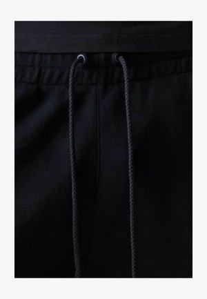 Pantalones o pantalones cortos de tela negra con cintura elástica y cordones negros atados a través de ojales metálicos en el centro frontal.