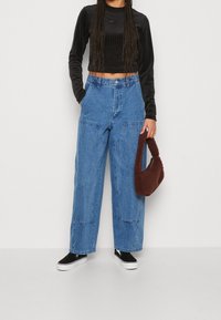 Blå denim vida byxor med framfickor, parat med en svart långärmad kort topp och en brun fluffig handväska. Svarta slipskor.