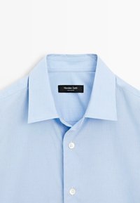 Chemise à rayures bleu clair avec col classique, cinq boutons et une étiquette indiquant "Massimo Dutti". Texture de tissu lisse.