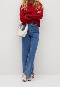 Czerwony sweter z prążkowanej tkaniny, szerokie niebieskie dżinsy, biała torba o zaokrąglonym kształcie oraz jasnoszare buty wsuwane o plecionym wyglądzie.