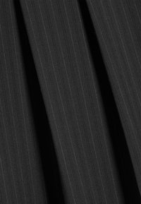 Gros plan d'un tissu foncé avec de fines rayures verticales et des plis visibles créant des ombres et de la texture.