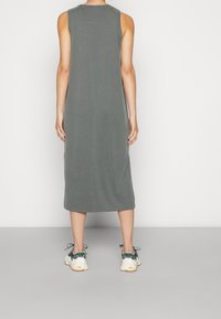 Mouwloze, knielange jurk van muted groene stof. Zachte textuur met een relaxte pasvorm. Gecombineerd met lichte sneakers, die een minimalistisch ontwerp tonen.