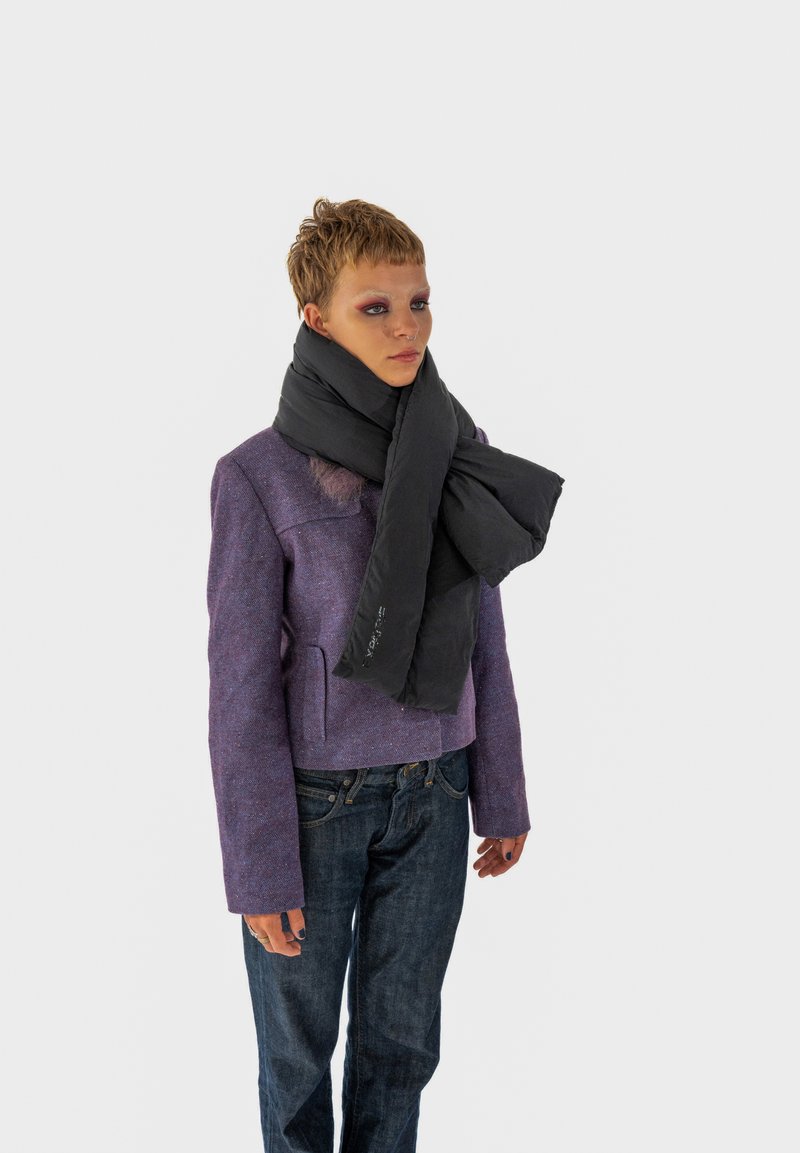 Sort tørklæde svunget omkring halsen, båret med en textured lilla jakke og mørke jeans. Tørklædet har en glat overflade og er oversized.