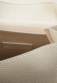 Beige bőr kézitáska belseje puha, világos bézs bélésű, texturált külső felülettel és fehér varrási részletekkel.