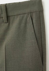 Gros plan d’un pantalon en tissu vert olive montrant la ceinture, la passants de ceinture et le détail de la poche avant inclinée.