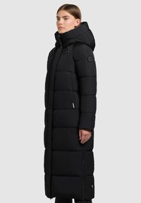 Cappotto lungo nero imbottito con colletto alto, motivo a quadrati, zip laterale e dettaglio del logo; realizzato in materiale isolante e resistente all'acqua.