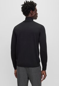Pull noir à col haut et manches longues, avec des poignets et un ourlet côtelés. Texture lisse, design ajusté et style minimaliste.