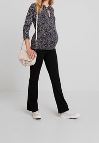 Graviditetstopp i marinblått med vita prickar, med knytning vid halsen och rynkade sidor. Bärs med svarta byxor och vita sneakers.