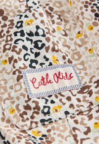 Gros plan d'une poche en tissu imprimé léopard avec de petites fleurs jaunes et une étiquette cousue "Cath Kids" en écriture rouge.