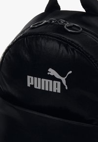 Zaino in nylon nero con forma arrotondata, chiusura a zip e logo Puma argentato. Include doppi manici e dettagli in superficie testurizzata.
