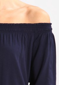 Granatowa bluzka odkrywająca ramiona z elastycznym dekoltem i długimi, luźnymi rękawami. Wykonana z miękkiego, lekkiego materiału o gładkiej fakturze.