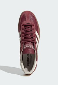 Bordo Adidas tenisica, izrađena od teksturirane kože i antilopa. Bijele pruge sa strane, okrugli vrh, podstavljeni ovratnik i gumeni potplat.
