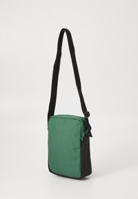 Piccola borsa a tracolla rettangolare con davanti verde e lati neri, dotata di una tracolla nera regolabile e chiusura con zip.