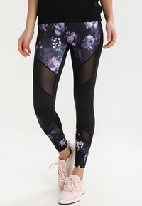 Zwarte bloemenleggings met paarse en witte patronen, voorzien van meshpanelen en een aangesloten ontwerp. Complementair met lichtroze sportschoenen.