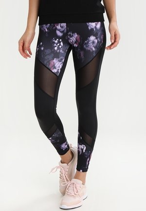 Zwarte bloemenleggings met paarse en witte patronen, voorzien van meshpanelen en een aangesloten ontwerp. Complementair met lichtroze sportschoenen.