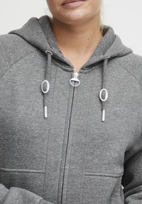 Gray zip-up hoodie made of soft fabric, featuring a drawstring hood, side pockets, and silver hardware details for the zipper and drawstrings.