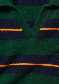 Dzianinowy pulower w zielono-granatowe paski z dekoltem w serek. Pomiędzy zieloną a granatową częścią znajduje się pomarańczowy pasek dla dodatkowego efektu. Miękka tekstura.