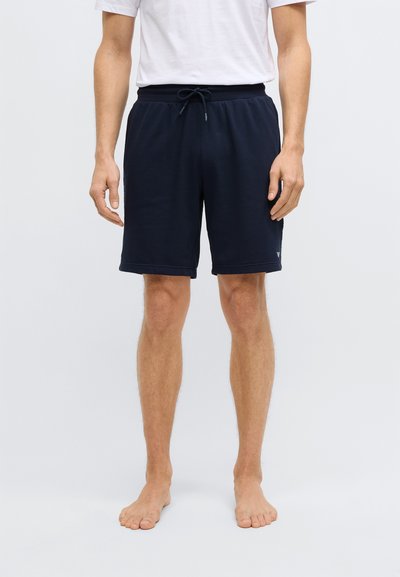 Tengerészkék sportnadrág elasztikus derékpánttal és húzózsinórral. Simább anyagból készült, oldalsó zsebekkel és a szegélynél található logórészlettel.