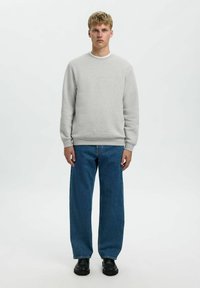 Un sweat-shirt gris avec col rond, des poignets côtelés, associé à un jean en denim bleu à jambes larges et des chaussures noires. Tissu simple et texturé.