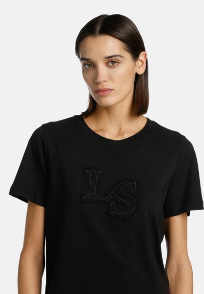 Black cotton t-shirt with crew neckline and short sleeves. Features textured black "LS" embroidery on the front. Simple, classic design.