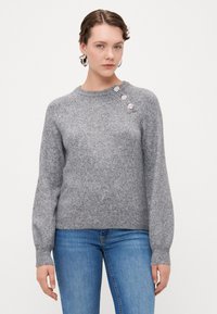 Grå strikket sweater med rund hals, tætsiddende ærmer og tre blomsterknapper på venstre skulder. Blød tekstur, afslappet design.