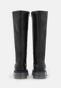 Bottes en cuir noires montantes jusqu'au genou avec des talons épais, translucides et massifs, fermeture éclair à l'arrière et embossage subtil de la marque près du haut.