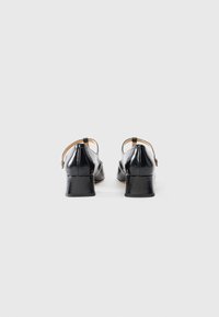 Black patent leather heels with a rounded toe and block heel. Features an adjustable ankle strap and smooth textured surface.