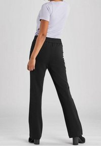 Svarta byxor med elastisk midja och rak bendesign. Mjuk tyg med en jämn textur, med sidofickor. Bärs tillsammans med en ljusgrå topp.