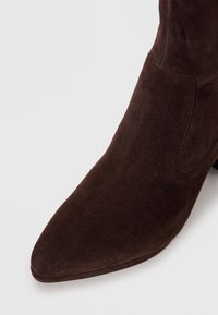 Brown suede ankle boot with a pointed toe, smooth texture, and a seamless design, featuring a stiletto heel for an elevated silhouette.
