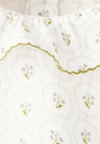 Vit tyg med ett intrikat blommönster, med gröna och grå accenter. Volangkrage med en skulpterad kant.