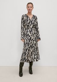 Langarmkleid mit einem schwarzen und cremefarbenen abstrakten Muster, V-Ausschnitt, tailliertem Bund und fließender Silhouette, kombiniert mit knielangen schwarzen Stiefeln.