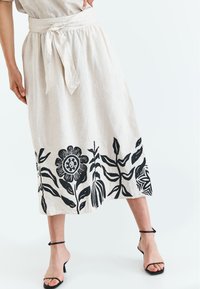 Linned midi-nederdel i beige med sorte blomster- og bladmønstre. Har en bundet talje og en flydende silhuet.