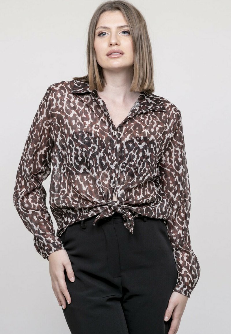 Blouse à imprimé léopard dans des tons de marron et de beige, avec des manches longues, un col, une fermeture à boutons sur le devant, et un détail de taille nouée.