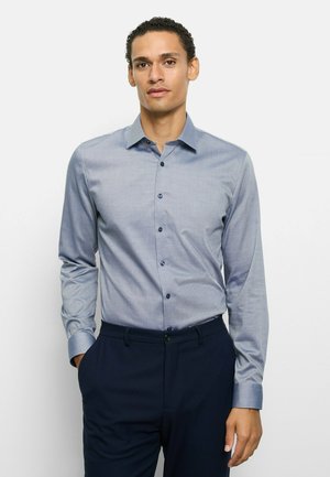 Hellblaues, knöpfbares Hemd mit feiner Struktur, tailliertem Schnitt und langen Ärmeln, kombiniert mit dunkelblauen Hosen. Verfügt über dunkle Knöpfe.