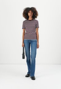 Bordeauxrode en witte gestreepte t-shirt, korte mouwen, gecombineerd met blauwe uitlopende jeans. Model draagt een gestructureerde zwarte handtas. Effen achtergrond.