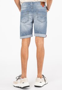 Lichtblauwe denim shorts met een omgeslagen zoom, met twee achterzakken en een leren label. Draagt met beige en witte sneakers.