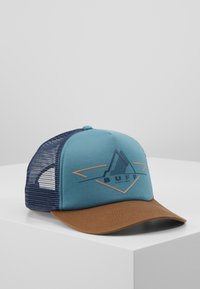Trucker cepure ar tirkīzu priekšpusi, brūnu zāli un tumši zilu sietu aizmugurē. Izrotāta ar ģeometrisku logo tumši zilā un brūnganā krāsā.
