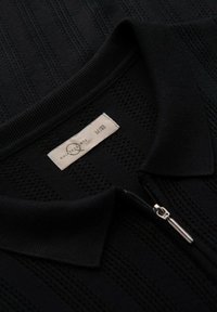 Black zip-up polo shirt with a textured knit pattern, ribbed collar, and a fabric label showing size M and brand logo.