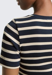 Granatowo-kremowa prążkowana bluzka z krótkim rękawem, o prążkowanej fakturze, z okrągłym dekoltem i detalami na szwach ramion.