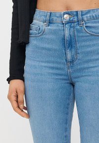 Høytlivs blå denimjeans med en glatt overflate, fem lommers design, metallknapp-lukking og subtil falming langs lårene.