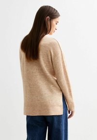 Maglione beige a maglia con una vestibilità rilassata, maniche lunghe e orlo a coste. Indossato sopra pantaloni larghi blu scuro, caratterizzati da una consistenza morbida.