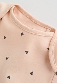 Puha rózsaszín babaruházat szórványosan fekete, apró szívmintákkal, bordázott nyakrésszel és vállszegéllyel.