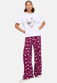 Hvid bomulds t-shirt med "Breakfast Club" grafik. Lilla pyjamabukser med mad- og drikke mønstre i hvid. Løs pasform.
