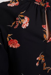Tessuto nero con stampa floreale rossa e arancione e dettagli arricciati vicino a uno spacco verticale che mostra la pelle sottostante.