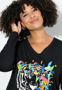 Zwarte lange mouwen V-hals shirt met een kleurrijk geometrisch patroon rond een witte tijgerafbeelding in het midden. Zachte textuur.