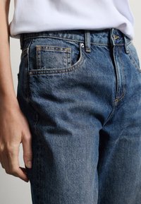 Jeans in denim blu con vita alta, cinque tasche e cuciture tono su tono. Presentano una trama sottile e un design classico in stile western.
